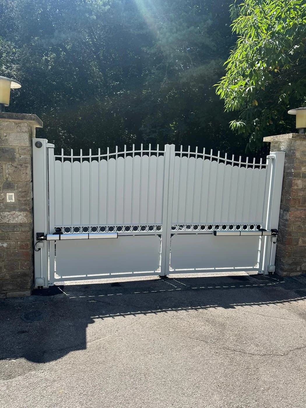 White electric driveway gates installed between stone pillars